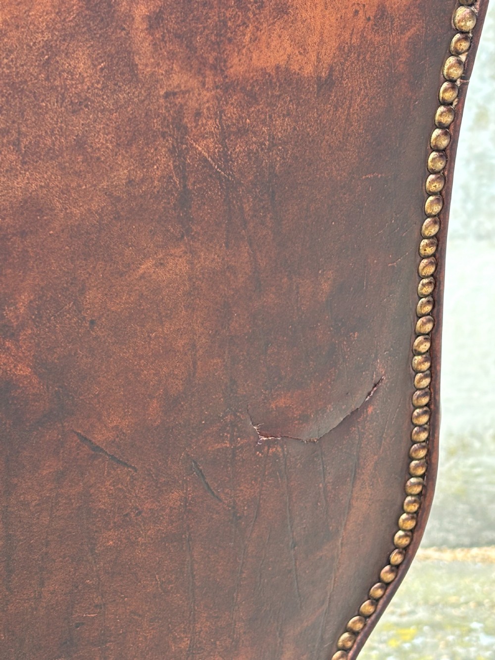 A 19th-century deep brown leather wingback armchair featuring a button-tufted backrest, brass stud trim, and hand-carved mahogany cabriole legs with ball-and-claw feet. View V