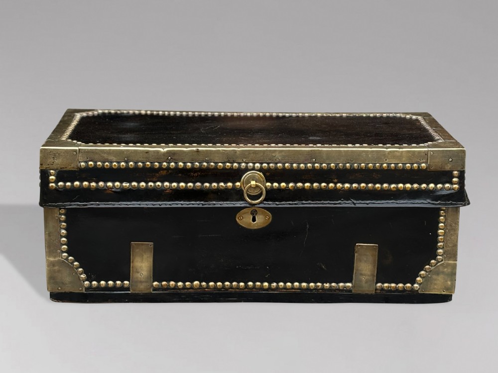 A 19th-century black leather coaching trunk featuring brass corner mounts, brass studding along the edges, side handles, and a central keyhole. View II
