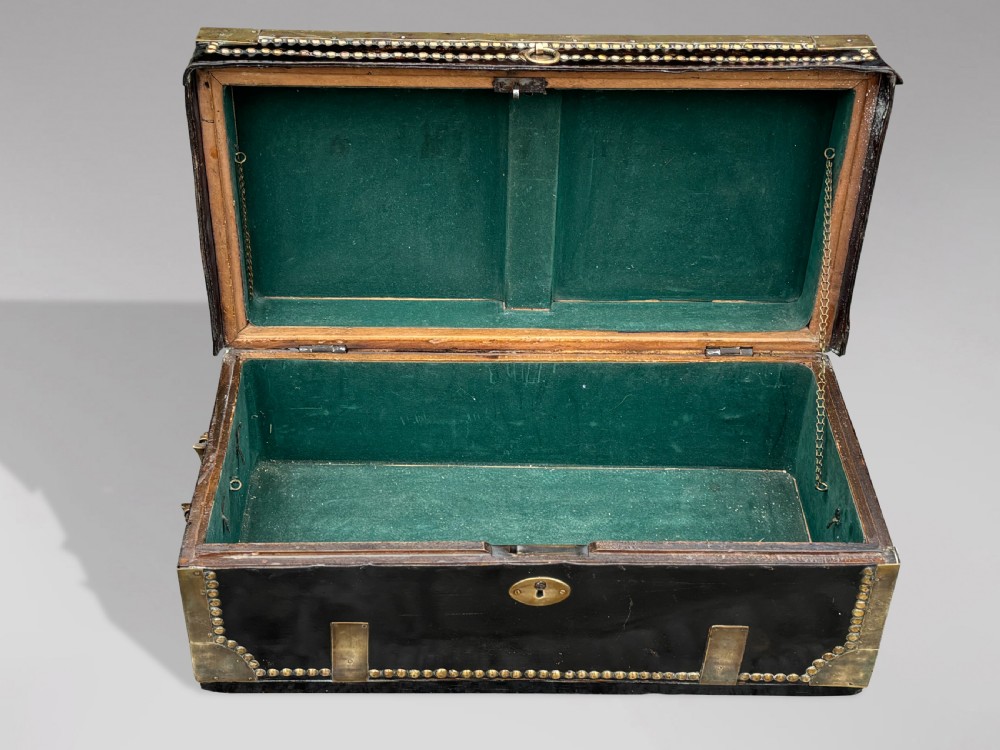 A 19th-century black leather coaching trunk featuring brass corner mounts, brass studding along the edges, side handles, and a central keyhole. View III