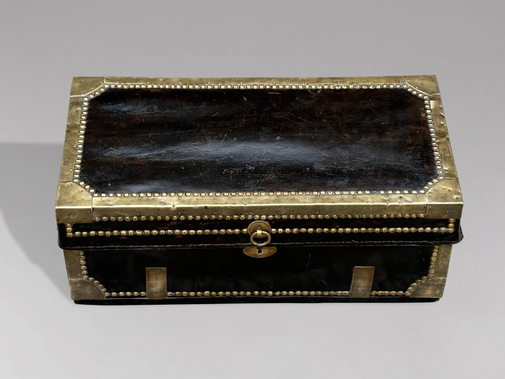 A 19th-century black leather coaching trunk featuring brass corner mounts, brass studding along the edges, side handles, and a central keyhole. View IV