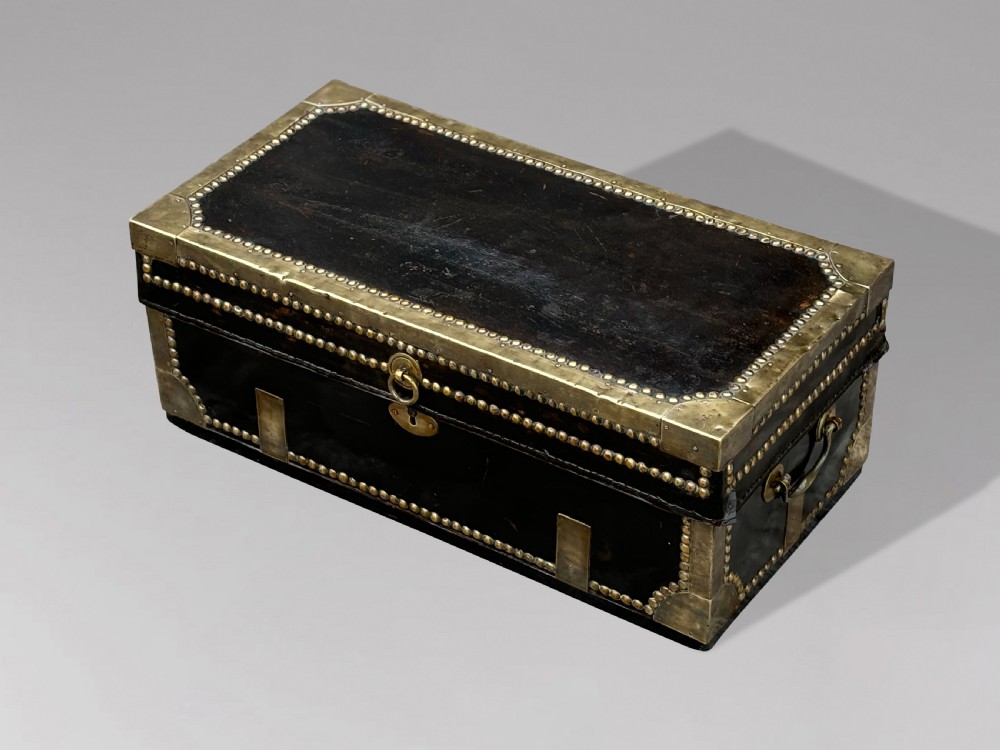 A 19th-century black leather coaching trunk featuring brass corner mounts, brass studding along the edges, side handles, and a central keyhole. View V