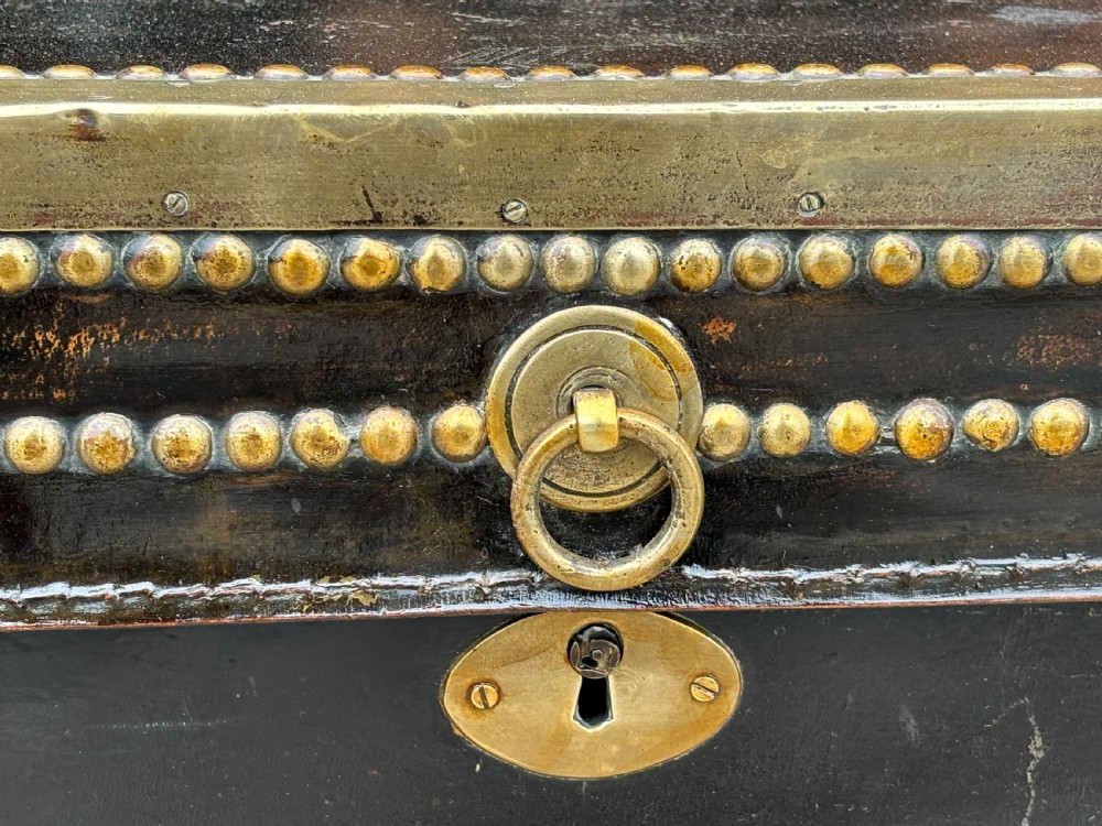 A 19th-century black leather coaching trunk featuring brass corner mounts, brass studding along the edges, side handles, and a central keyhole. View VII