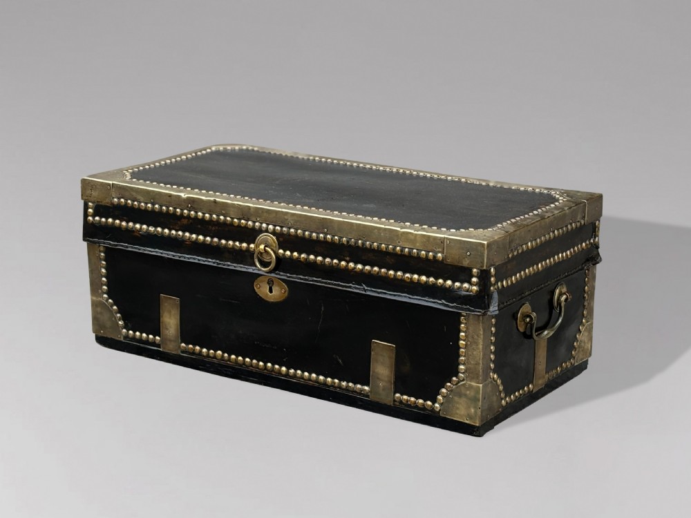 A 19th-century black leather coaching trunk featuring brass corner mounts, brass studding along the edges, side handles, and a central keyhole. View VIII