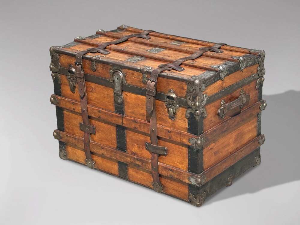 A 19th-century rectangular pine travelling trunk with metal corner protectors, horizontal wooden reinforcement slats, metal latches, and dual leather straps.