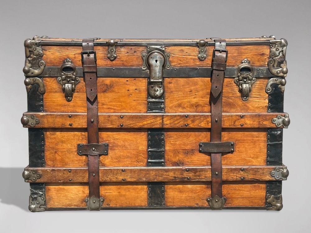 A 19th-century rectangular pine travelling trunk with metal corner protectors, horizontal wooden reinforcement slats, metal latches, and dual leather straps. View VI
