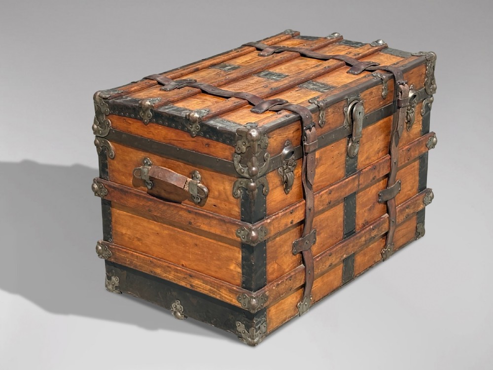 A 19th-century rectangular pine travelling trunk with metal corner protectors, horizontal wooden reinforcement slats, metal latches, and dual leather straps. View X