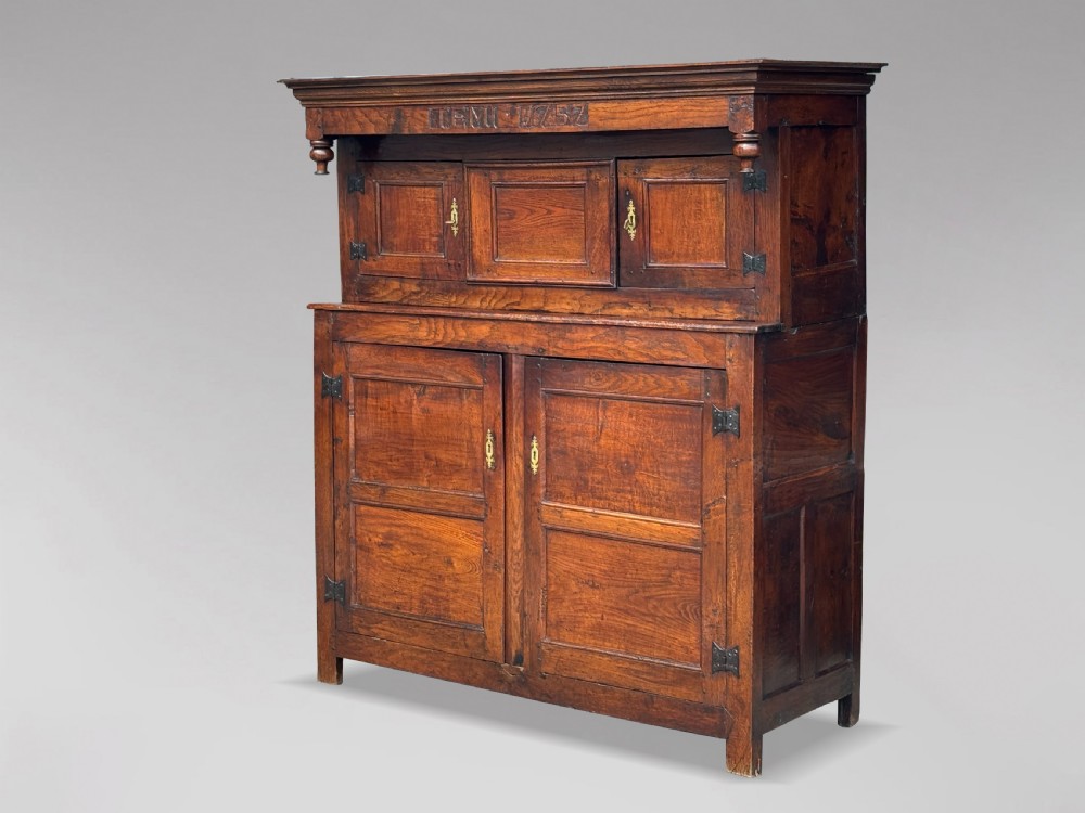 An 18th-century dark elm court cupboard with carved date inscription, panelled doors, brass escutcheons, and iron hinges. View II