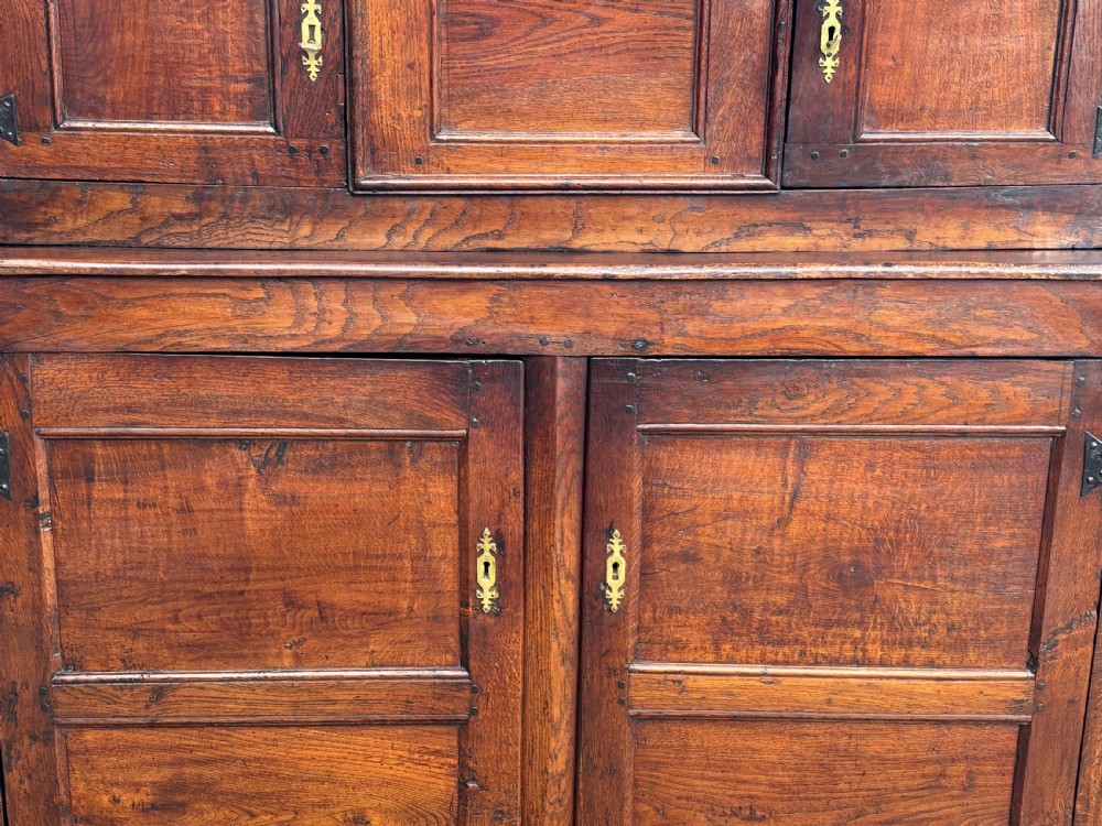 An 18th-century dark elm court cupboard with carved date inscription, panelled doors, brass escutcheons, and iron hinges. View IV
