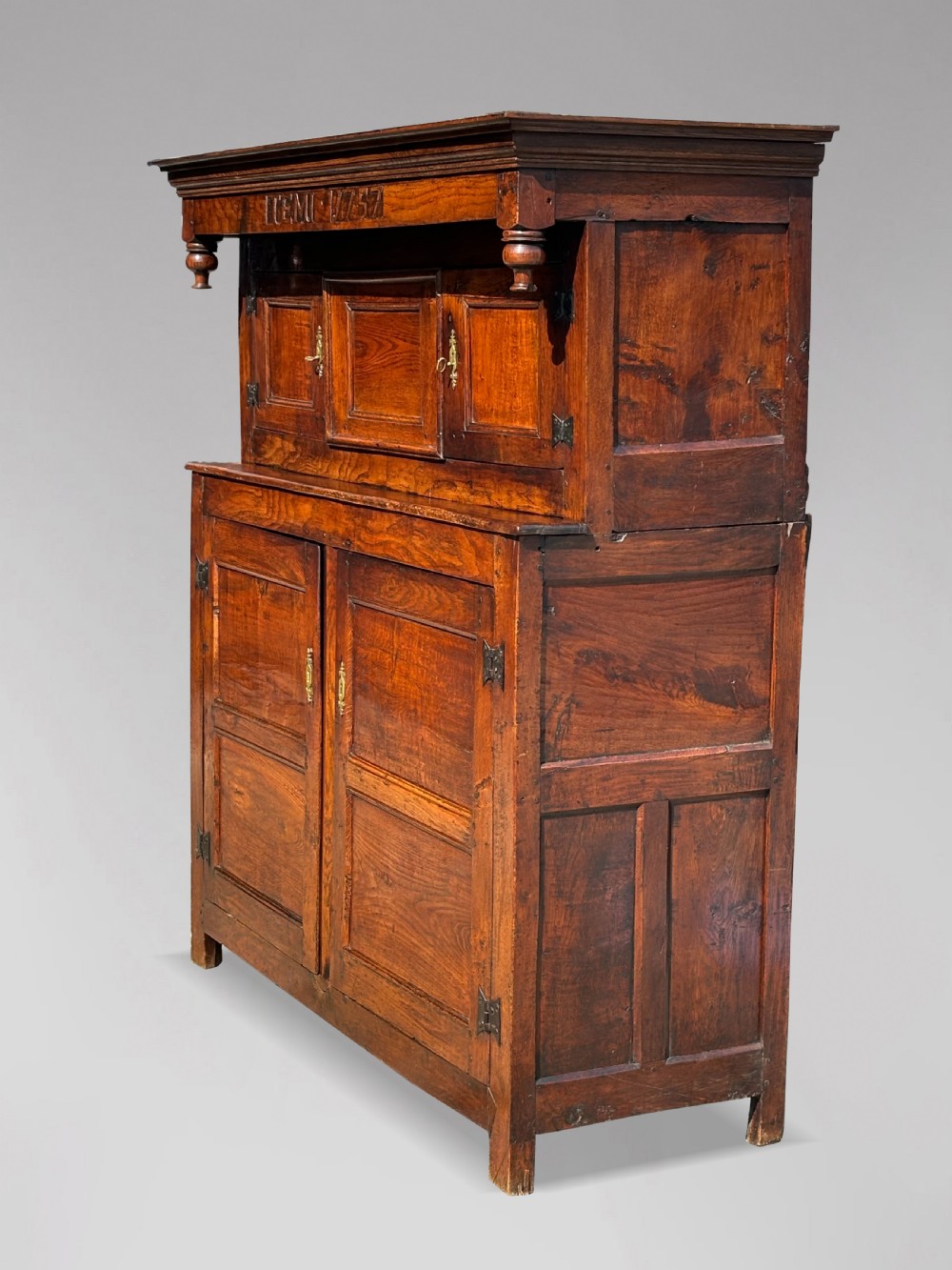 An 18th-century dark elm court cupboard with carved date inscription, panelled doors, brass escutcheons, and iron hinges. View VI