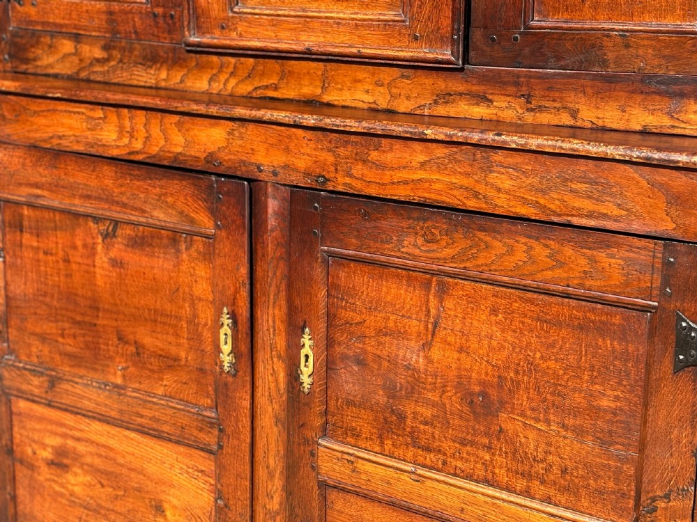 An 18th-century dark elm court cupboard with carved date inscription, panelled doors, brass escutcheons, and iron hinges. View VIII