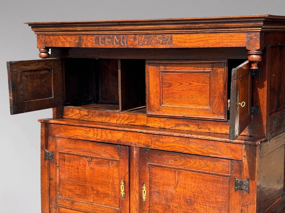 An 18th-century dark elm court cupboard with carved date inscription, panelled doors, brass escutcheons, and iron hinges. View IX