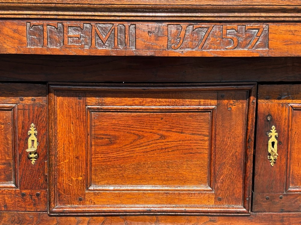 An 18th-century dark elm court cupboard with carved date inscription, panelled doors, brass escutcheons, and iron hinges. View X