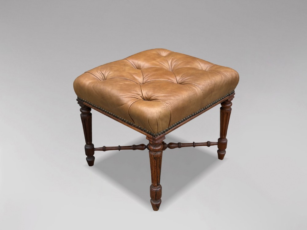 A 19th-century Regency period stool featuring a button-tufted tan leather seat with brass stud trimming, supported by turned fluted rosewood legs and turned stretchers.