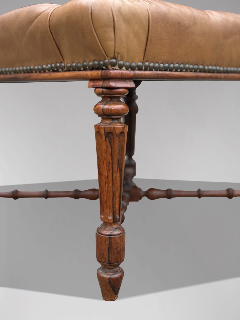 A 19th-century Regency period stool featuring a button-tufted tan leather seat with brass stud trimming, supported by turned fluted rosewood legs and turned stretchers. View VI