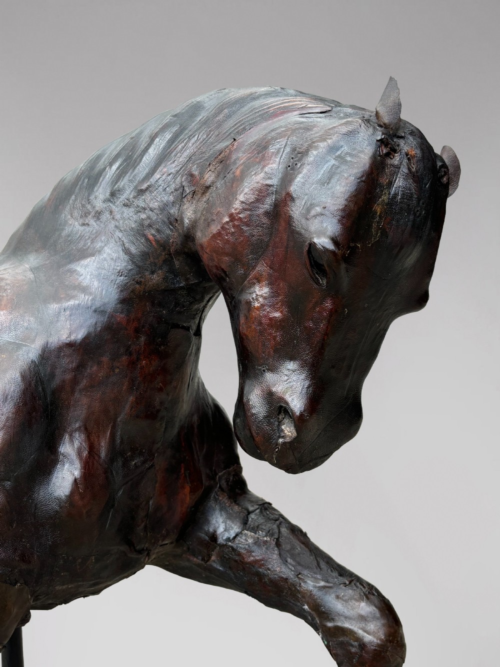 A dark brown hand-stitched leather model of a horse in a trotting pose with one front leg raised. View IV