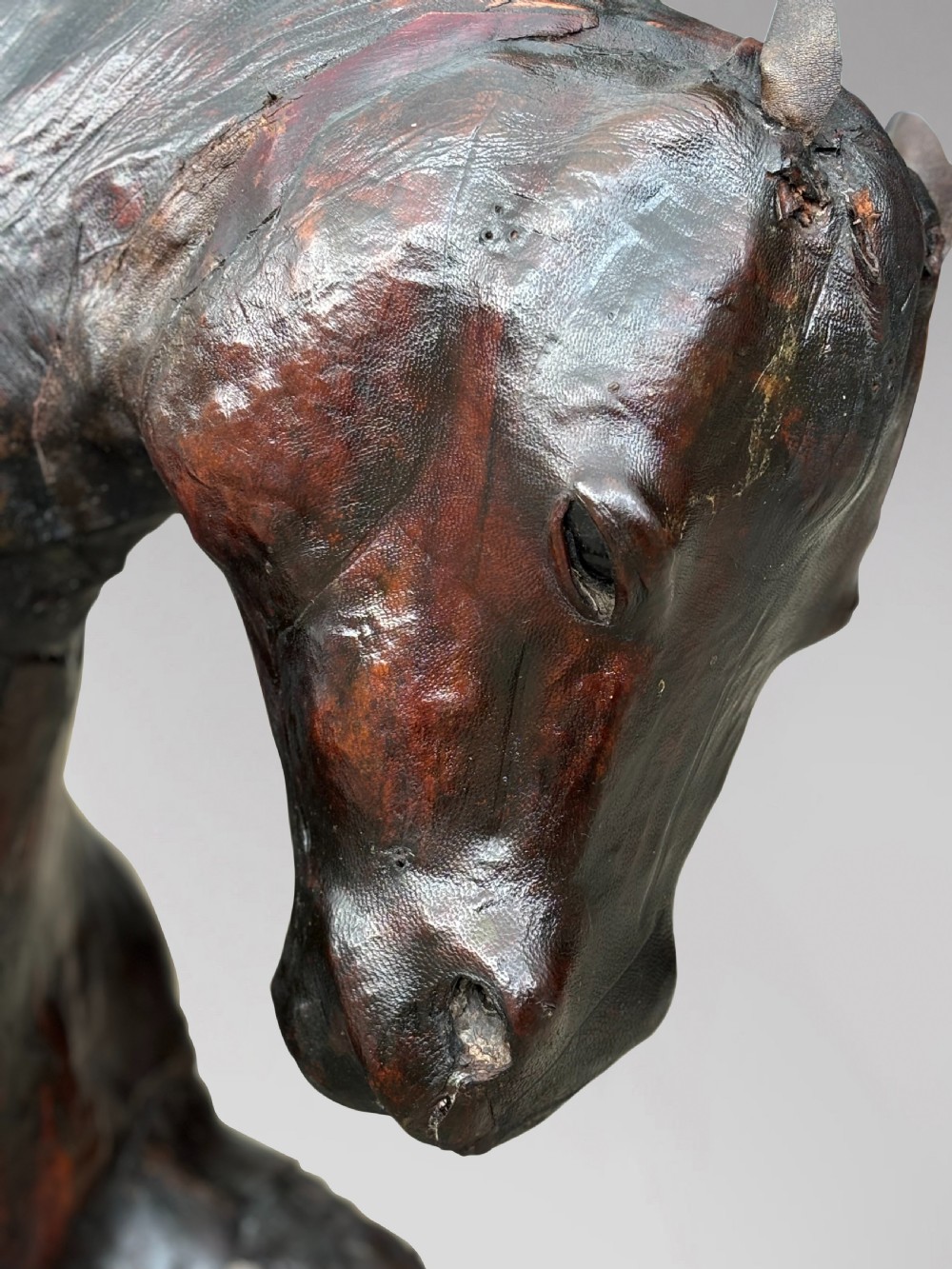 A dark brown hand-stitched leather model of a horse in a trotting pose with one front leg raised. View VI