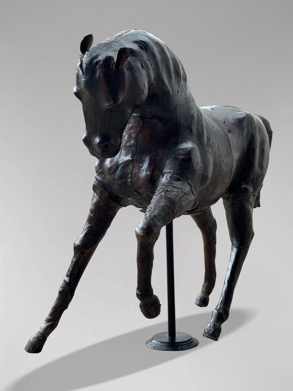 A dark brown hand-stitched leather model of a horse in a trotting pose with one front leg raised. View VII