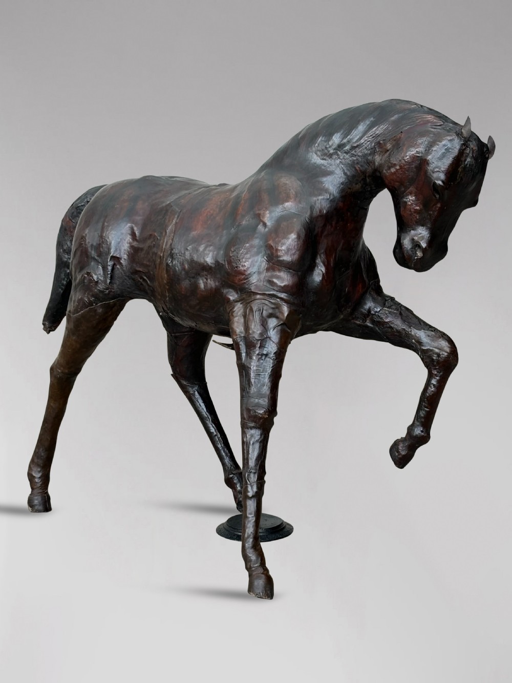 A dark brown hand-stitched leather model of a horse in a trotting pose with one front leg raised. View VIII