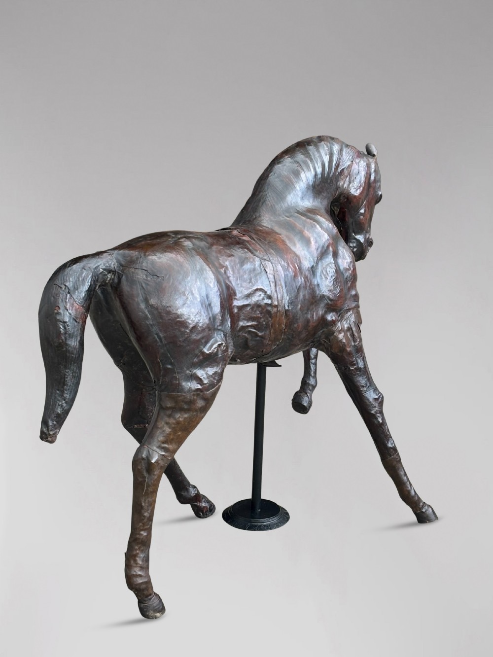 A dark brown hand-stitched leather model of a horse in a trotting pose with one front leg raised. View IX