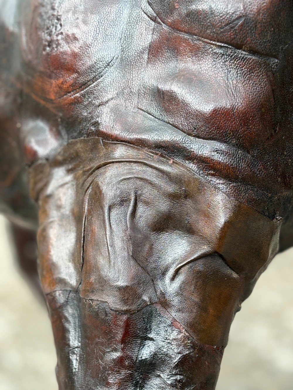 A dark brown hand-stitched leather model of a horse in a trotting pose with one front leg raised. View XI