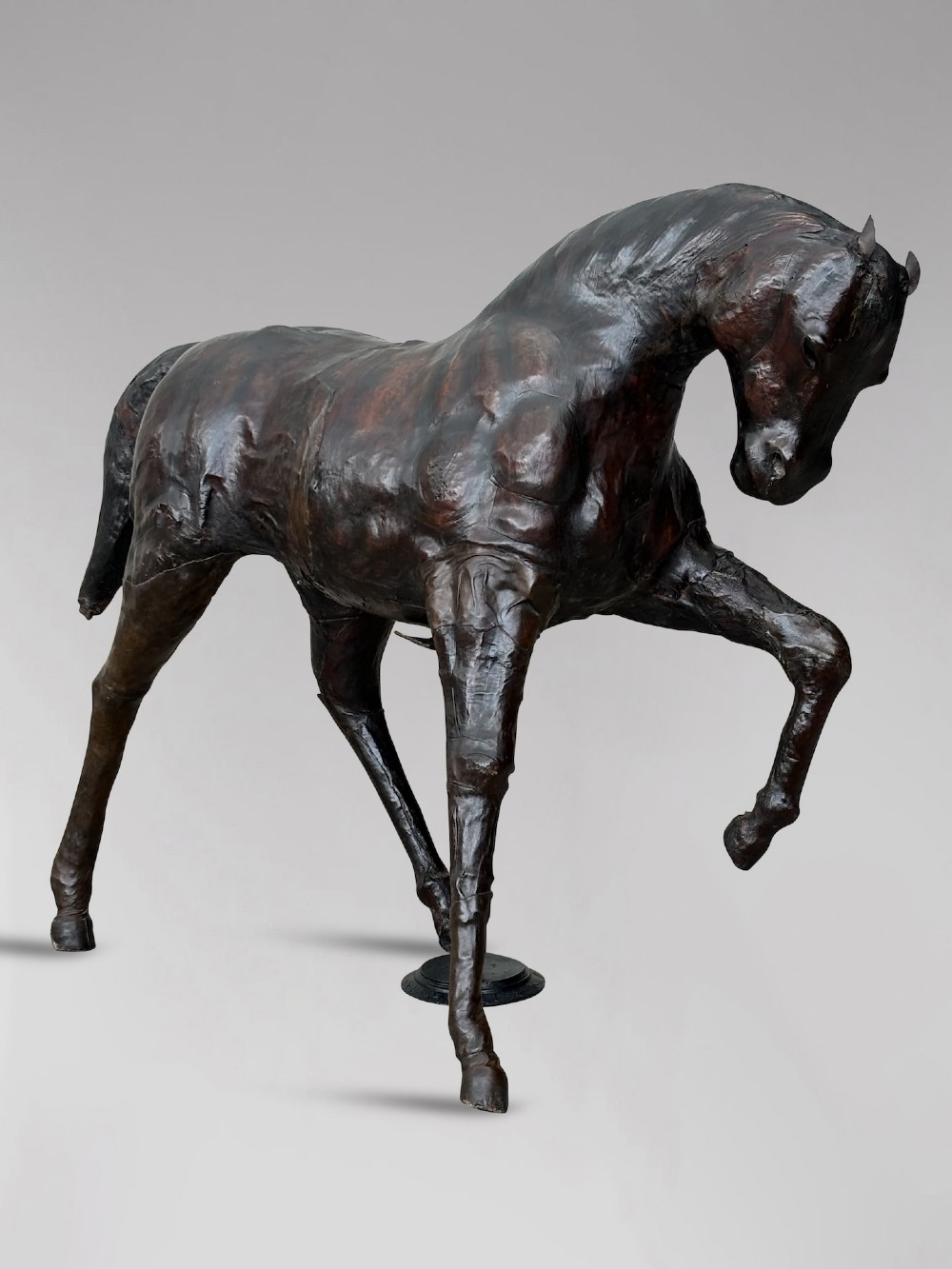A dark brown hand-stitched leather model of a horse in a trotting pose with one front leg raised.
