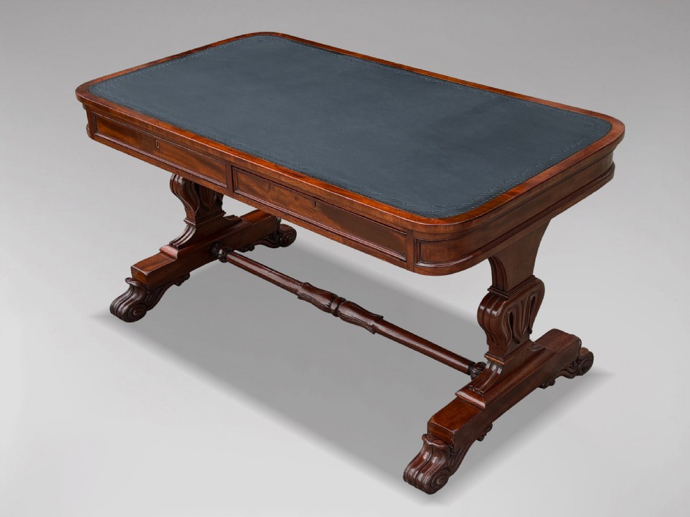 A 19th-century William IV mahogany writing table featuring a dark leather inset top, frieze drawers, carved trestle supports, and scroll feet.