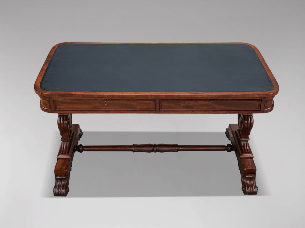 A 19th-century William IV mahogany writing table featuring a dark leather inset top, frieze drawers, carved trestle supports, and scroll feet. View II