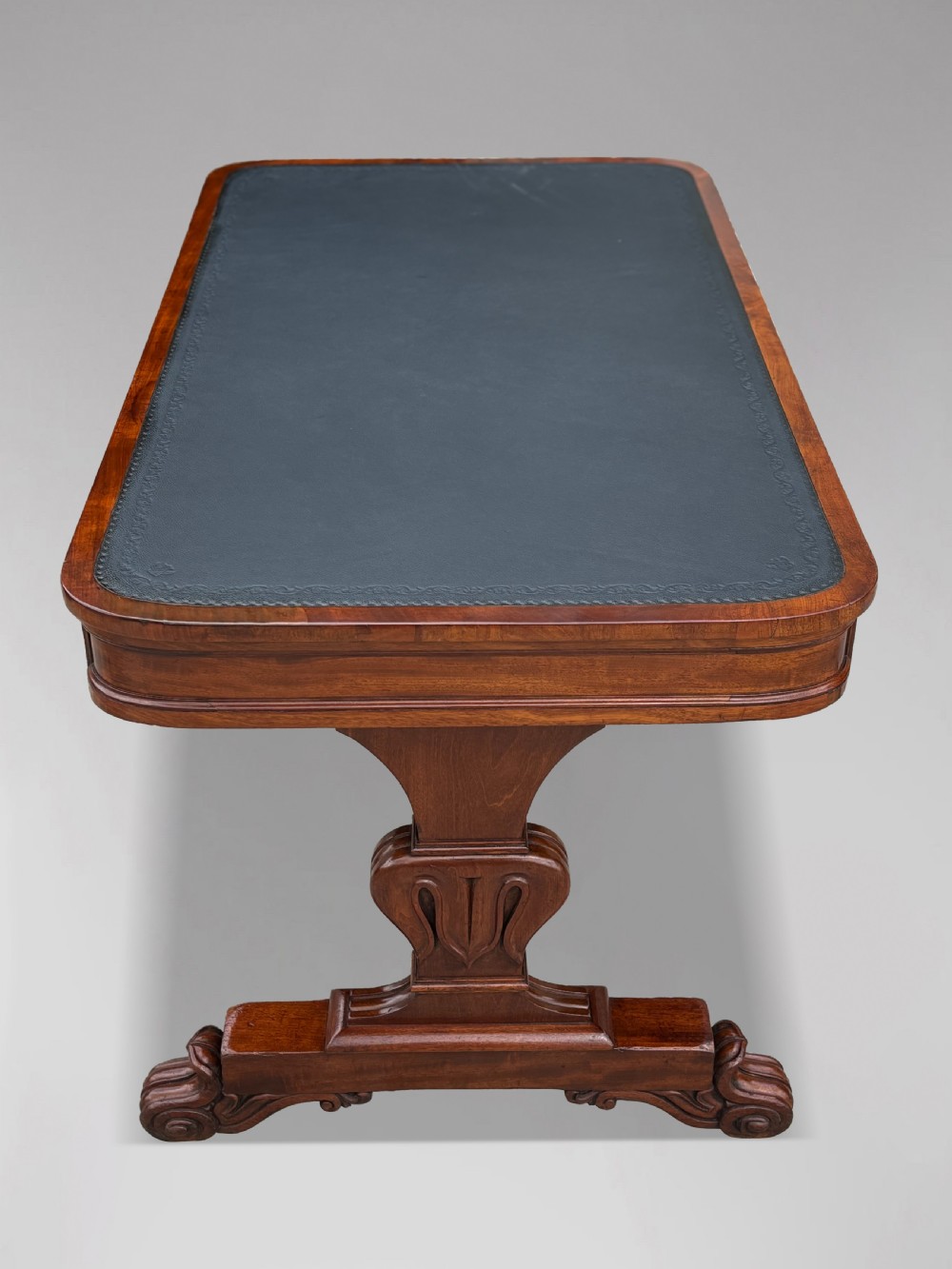 A 19th-century William IV mahogany writing table featuring a dark leather inset top, frieze drawers, carved trestle supports, and scroll feet. View III