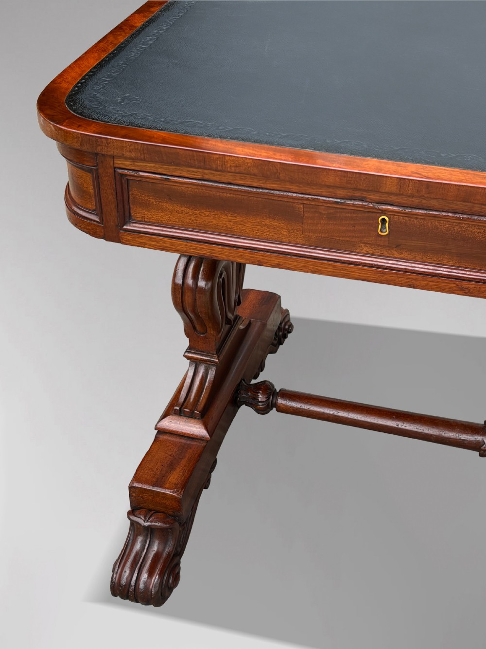 A 19th-century William IV mahogany writing table featuring a dark leather inset top, frieze drawers, carved trestle supports, and scroll feet. View V