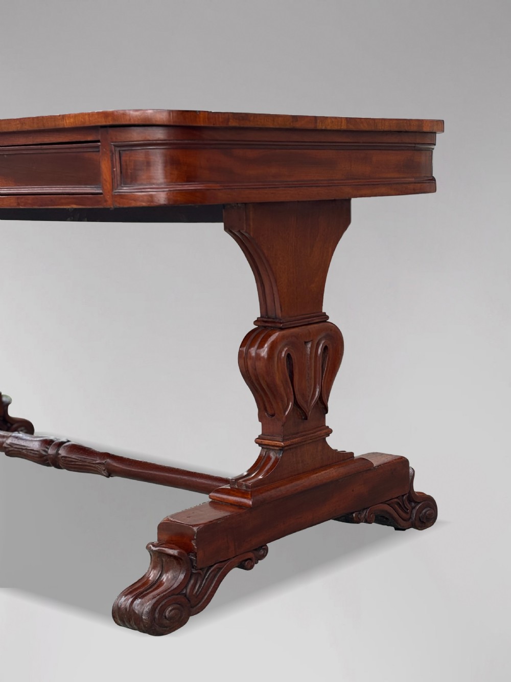 A 19th-century William IV mahogany writing table featuring a dark leather inset top, frieze drawers, carved trestle supports, and scroll feet. View VI