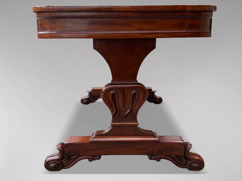 A 19th-century William IV mahogany writing table featuring a dark leather inset top, frieze drawers, carved trestle supports, and scroll feet. View VII