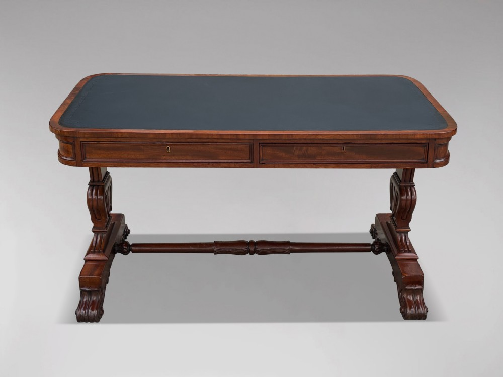 A 19th-century William IV mahogany writing table featuring a dark leather inset top, frieze drawers, carved trestle supports, and scroll feet. View X