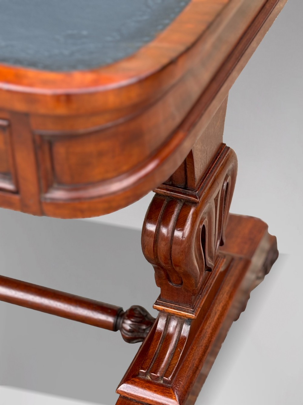 A 19th-century William IV mahogany writing table featuring a dark leather inset top, frieze drawers, carved trestle supports, and scroll feet. View XI