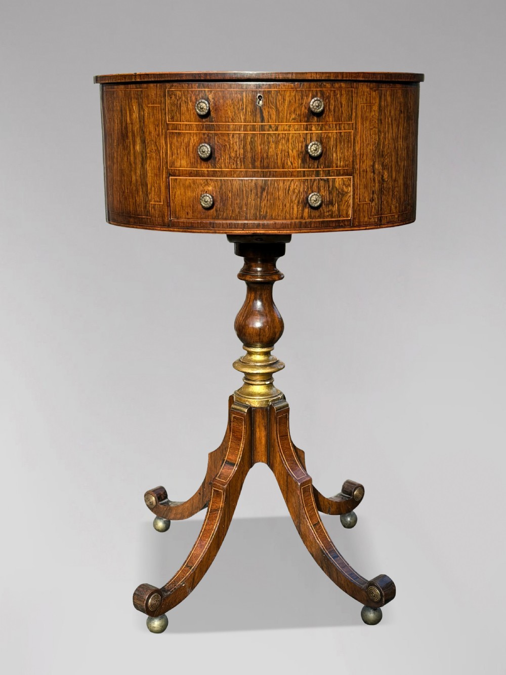A 19th-century Regency rosewood circular work table featuring drawer fronts with brass knobs, a turned central stem, and a tripod base on ball feet.