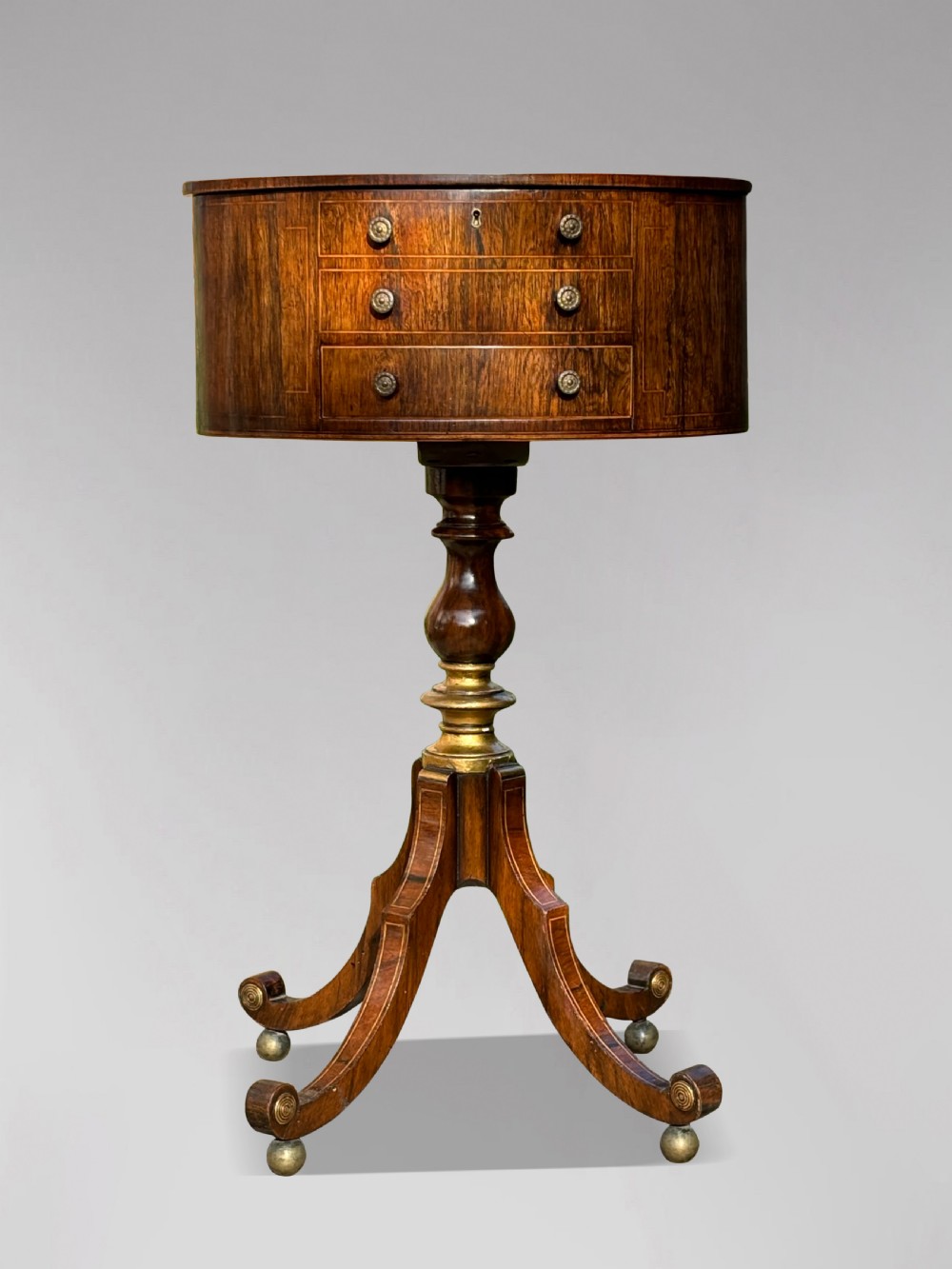 A 19th-century Regency rosewood circular work table featuring drawer fronts with brass knobs, a turned central stem, and a tripod base on ball feet. View X