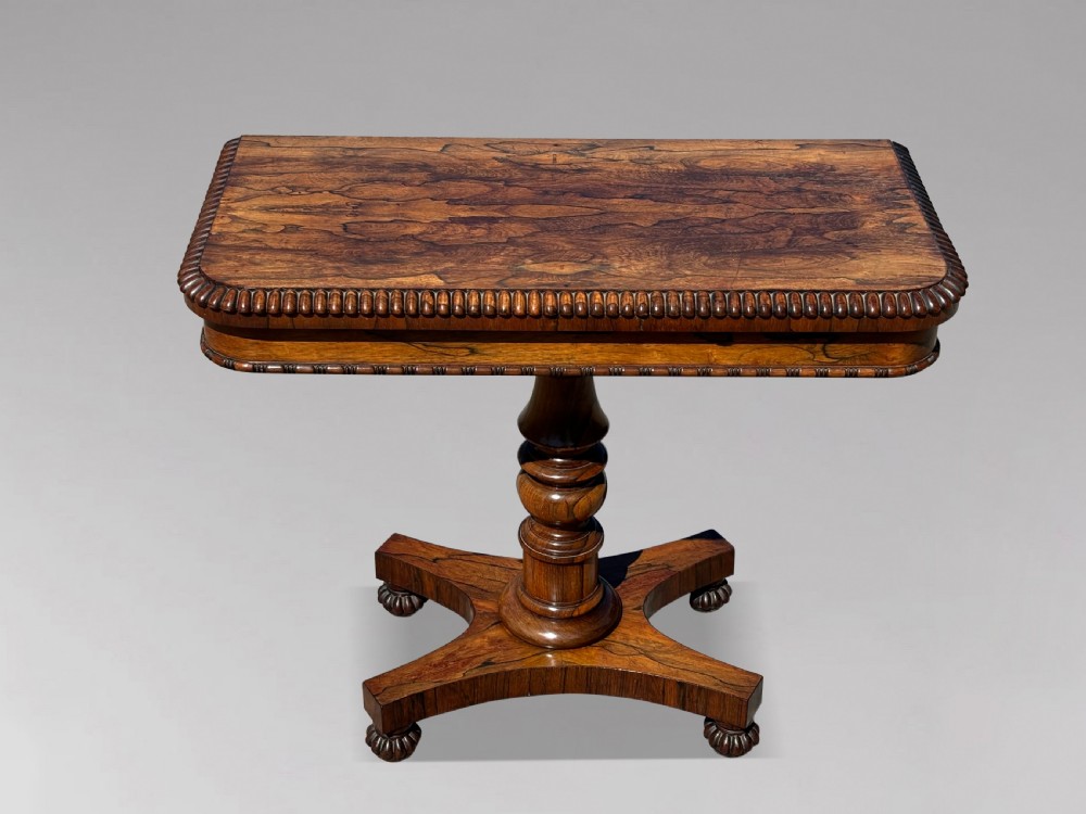 A 19th-century William IV rosewood fold-over card table featuring a gadrooned rim, a turned column stem, and a concave platform base with carved feet.
