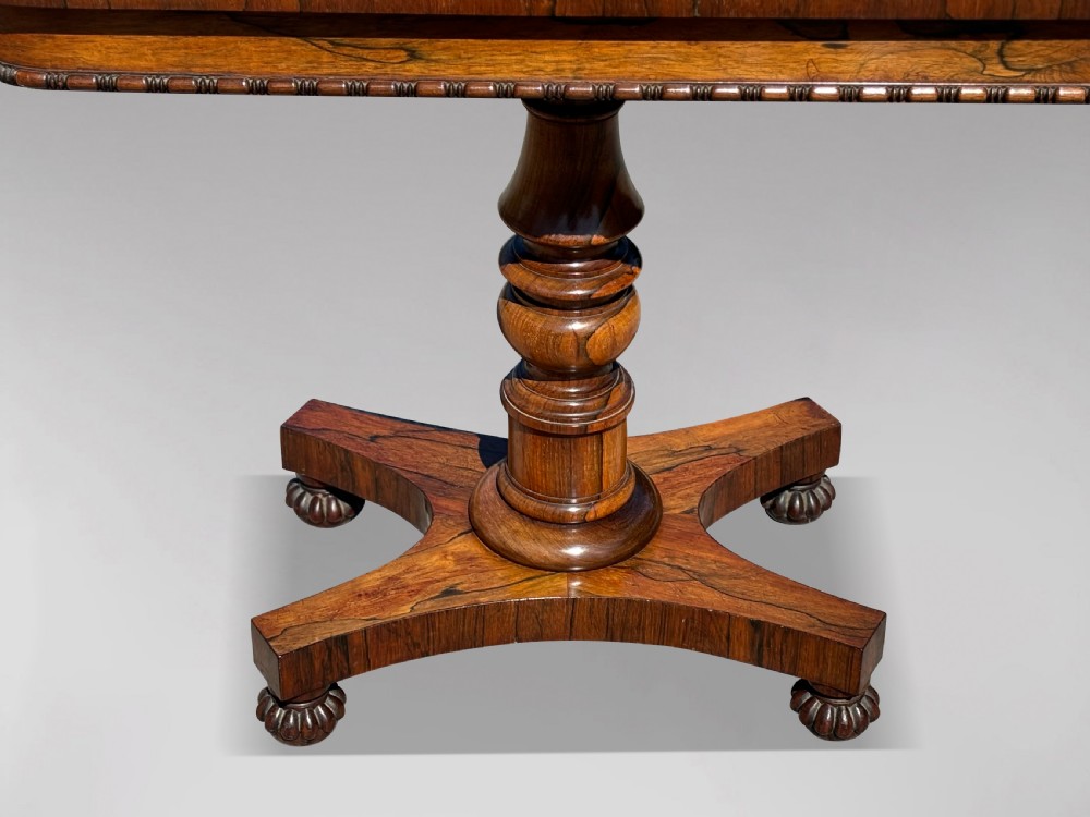 A 19th-century William IV rosewood fold-over card table featuring a gadrooned rim, a turned column stem, and a concave platform base with carved feet. View VII