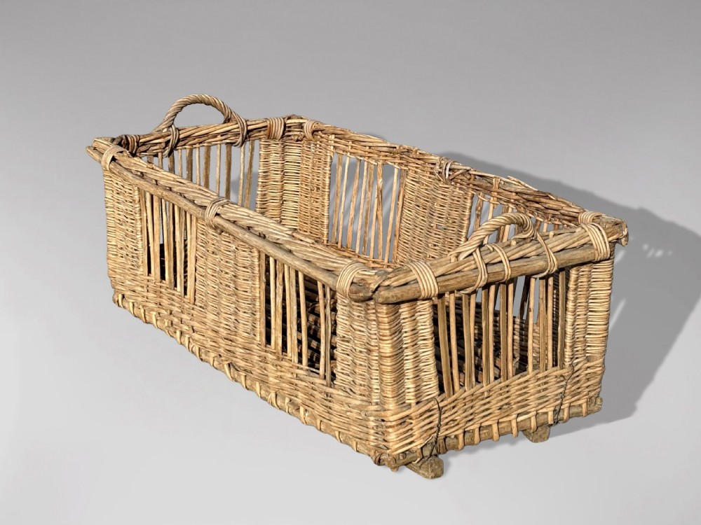A large rectangular French wicker basket featuring open vertical weave, woven loop handles, and wooden runner skids along the base.
