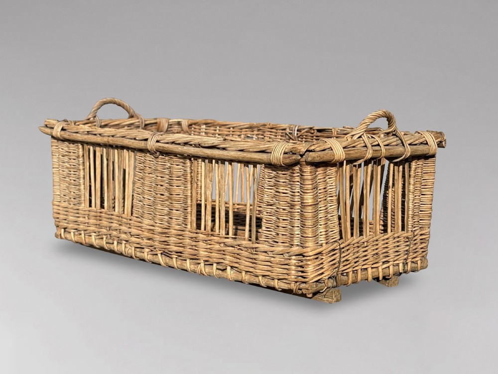A large rectangular French wicker basket featuring open vertical weave, woven loop handles, and wooden runner skids along the base. View V