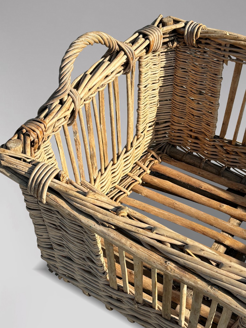 A large rectangular French wicker basket featuring open vertical weave, woven loop handles, and wooden runner skids along the base. View VI