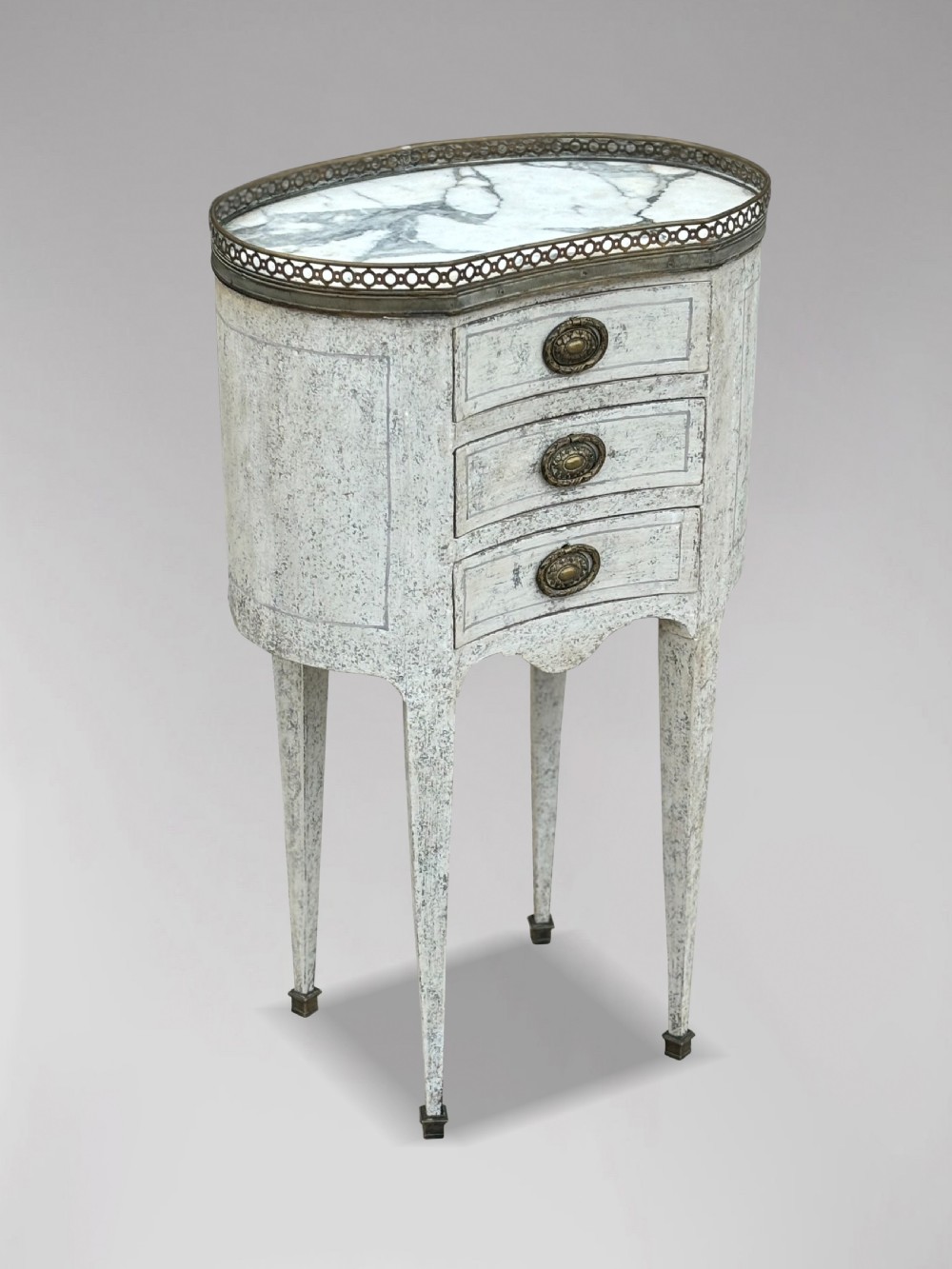An early 20th-century French Louis XVI style oval night table with distressed grey paintwork, three small drawers, brass pull handles, a marble inset top, and a brass gallery rail.