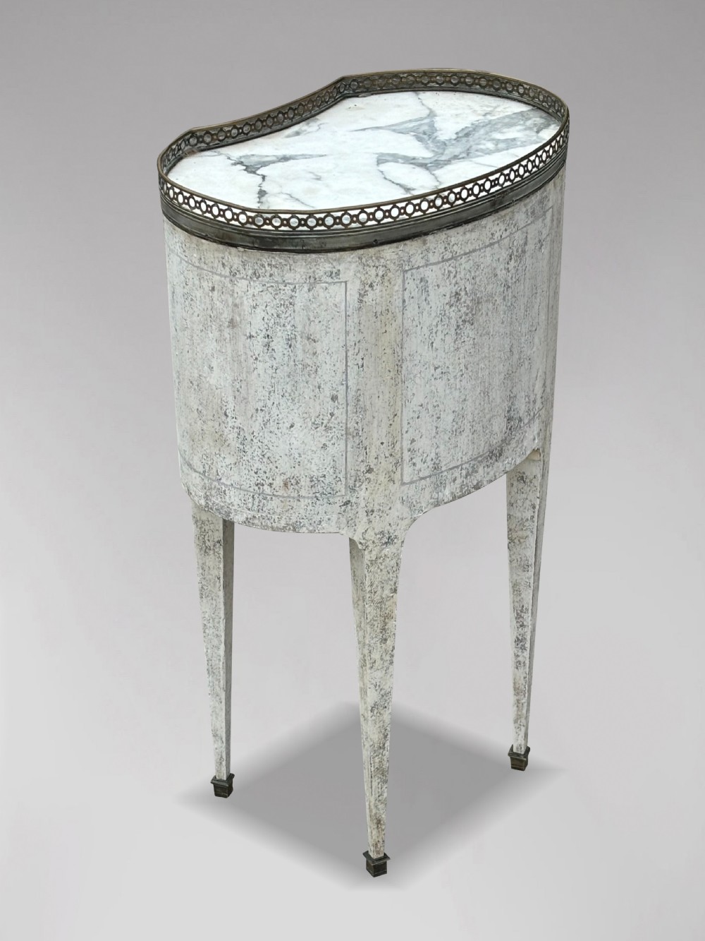 An early 20th-century French Louis XVI style oval night table with distressed grey paintwork, three small drawers, brass pull handles, a marble inset top, and a brass gallery rail. View IV