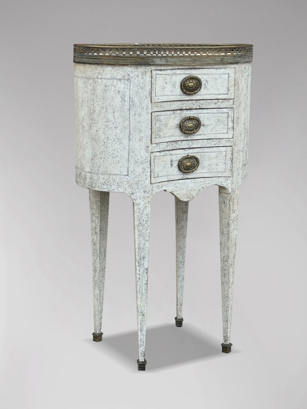 An early 20th-century French Louis XVI style oval night table with distressed grey paintwork, three small drawers, brass pull handles, a marble inset top, and a brass gallery rail. View IX