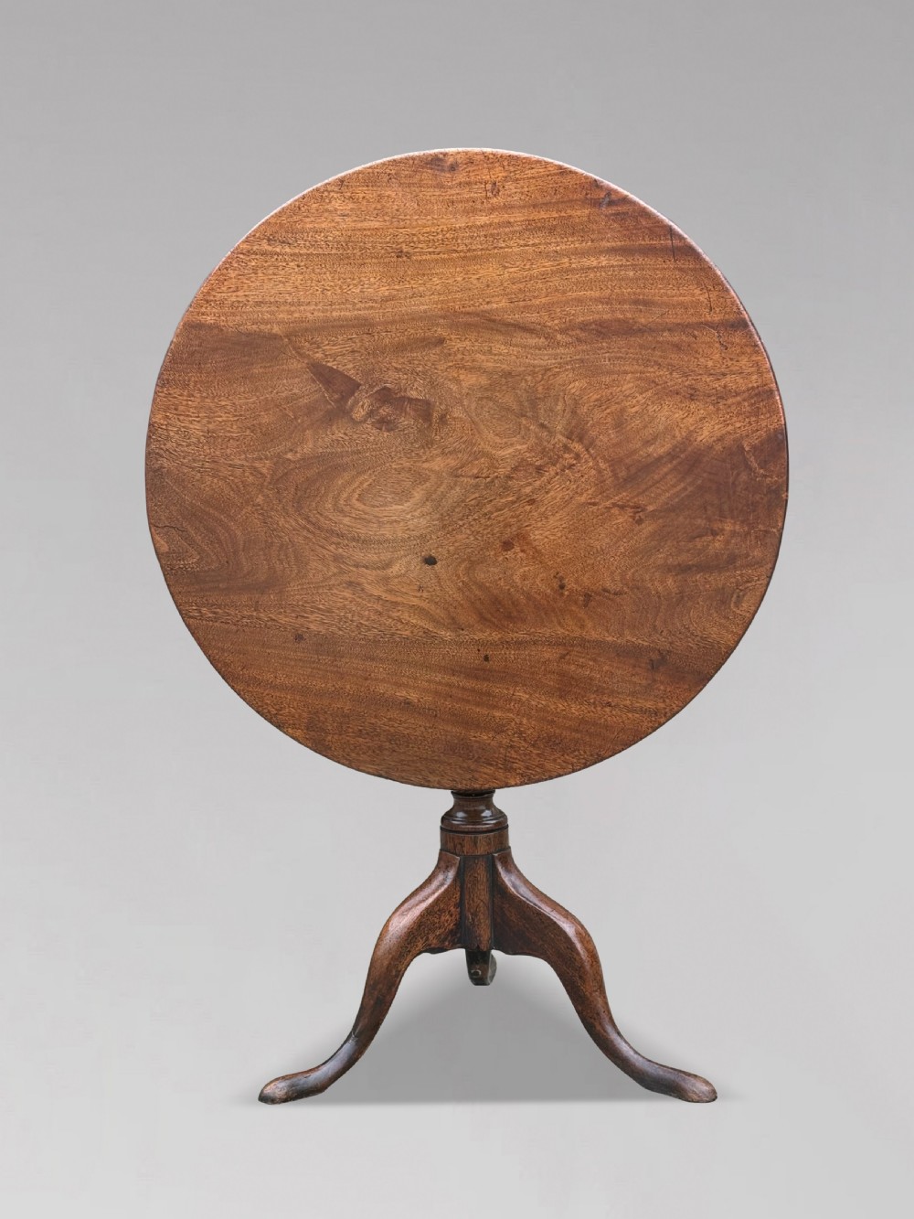 An 18th-century George III mahogany tripod table with its circular top tilted vertically above a turned central column and three cabriole legs.