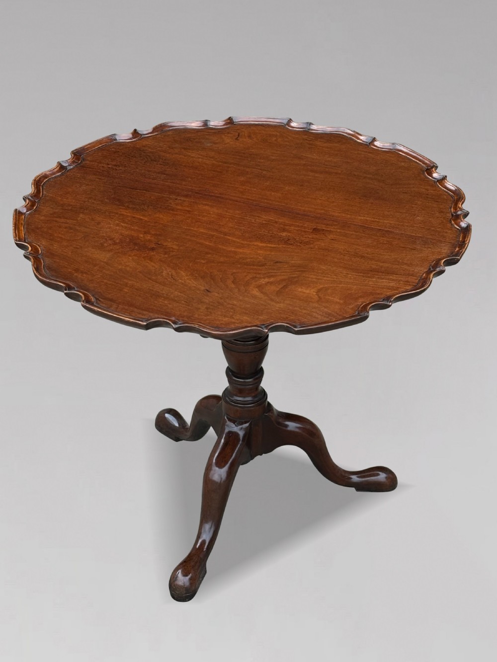 An 18th-century George III mahogany tilt-top tripod table shown in the vertical position with a carved pie-crust rim, turned pedestal, and cabriole legs. View V