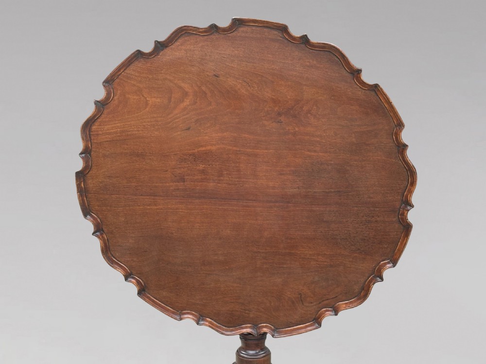 An 18th-century George III mahogany tilt-top tripod table shown in the vertical position with a carved pie-crust rim, turned pedestal, and cabriole legs. View VI