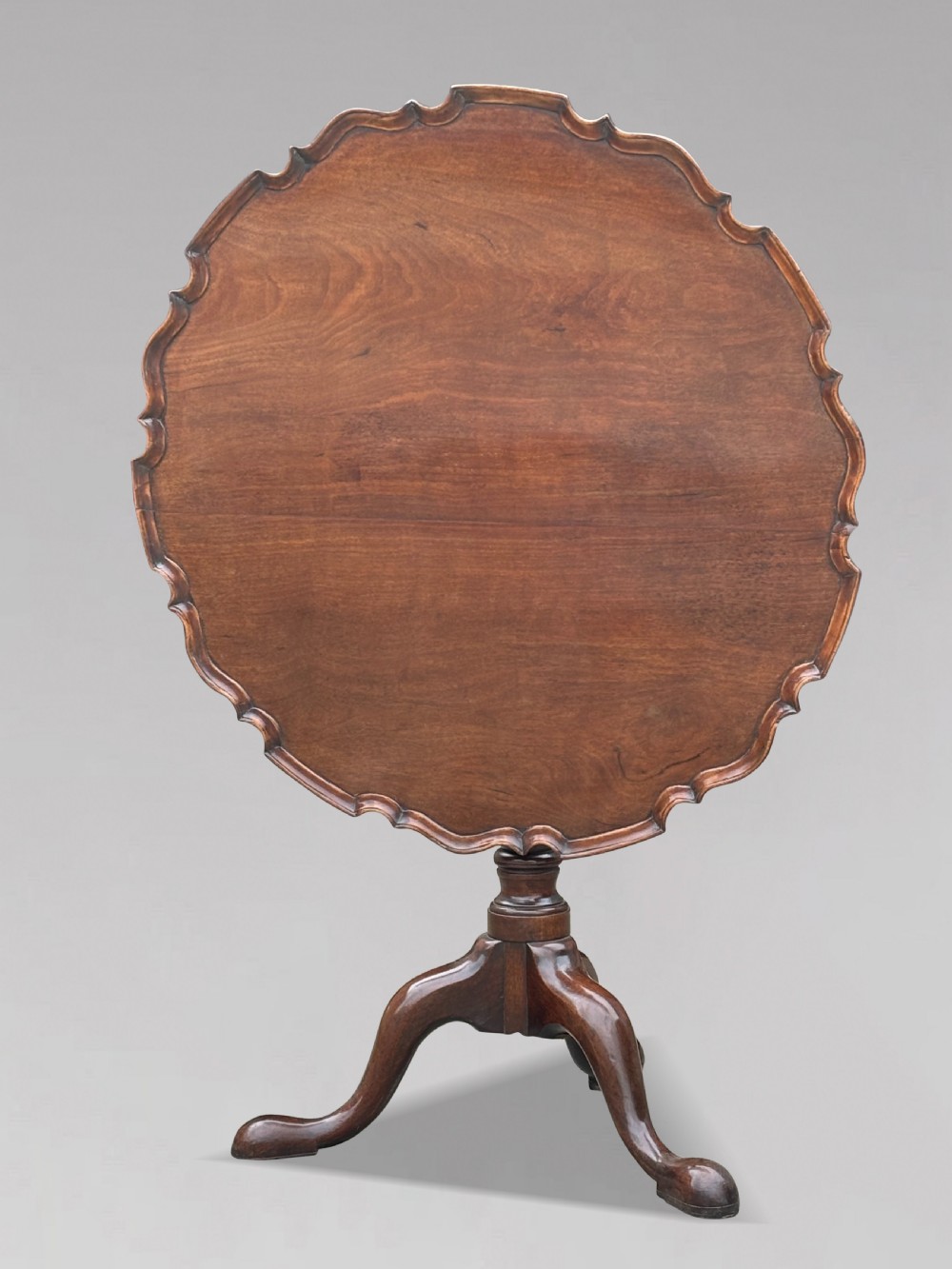 An 18th-century George III mahogany tilt-top tripod table shown in the vertical position with a carved pie-crust rim, turned pedestal, and cabriole legs. View VIII