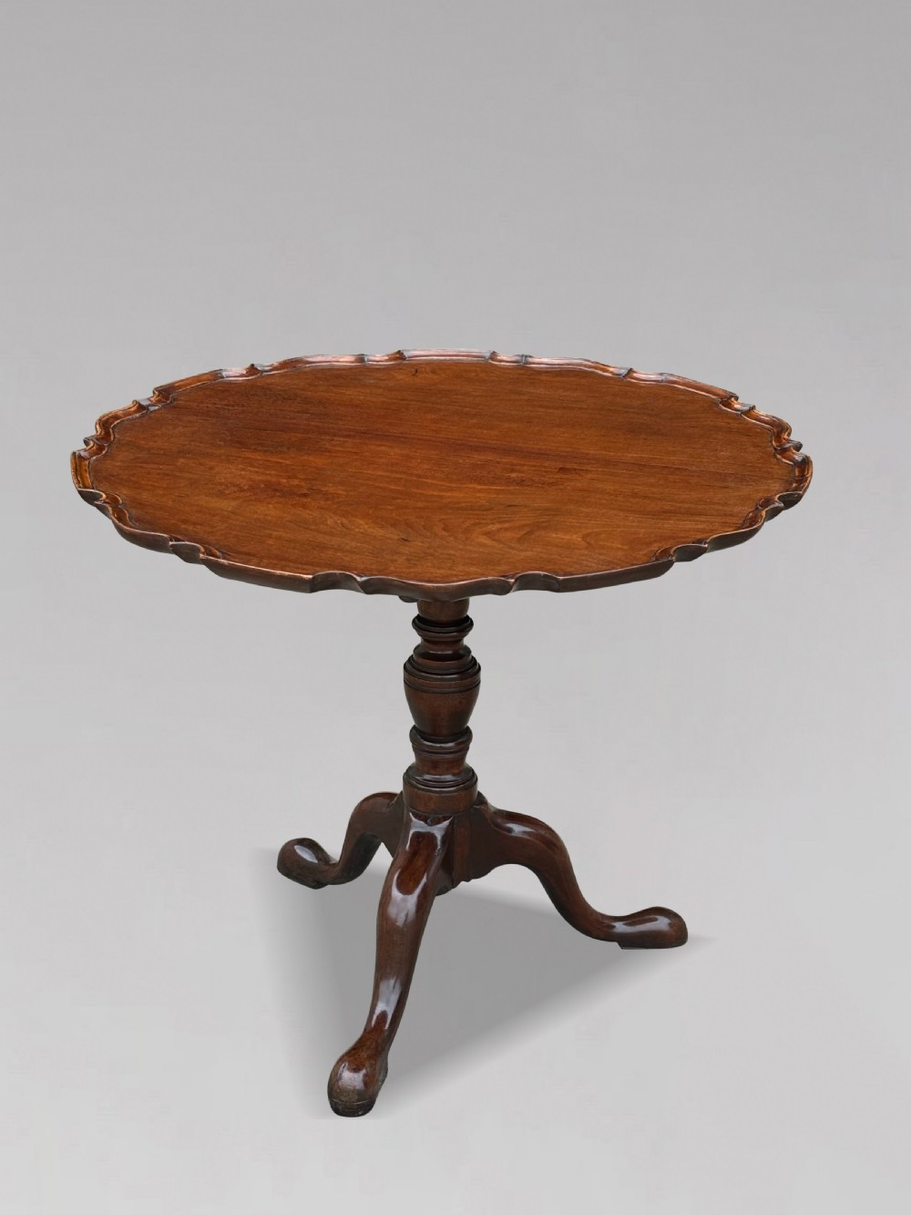 An 18th-century George III mahogany tilt-top tripod table shown in the vertical position with a carved pie-crust rim, turned pedestal, and cabriole legs. View X