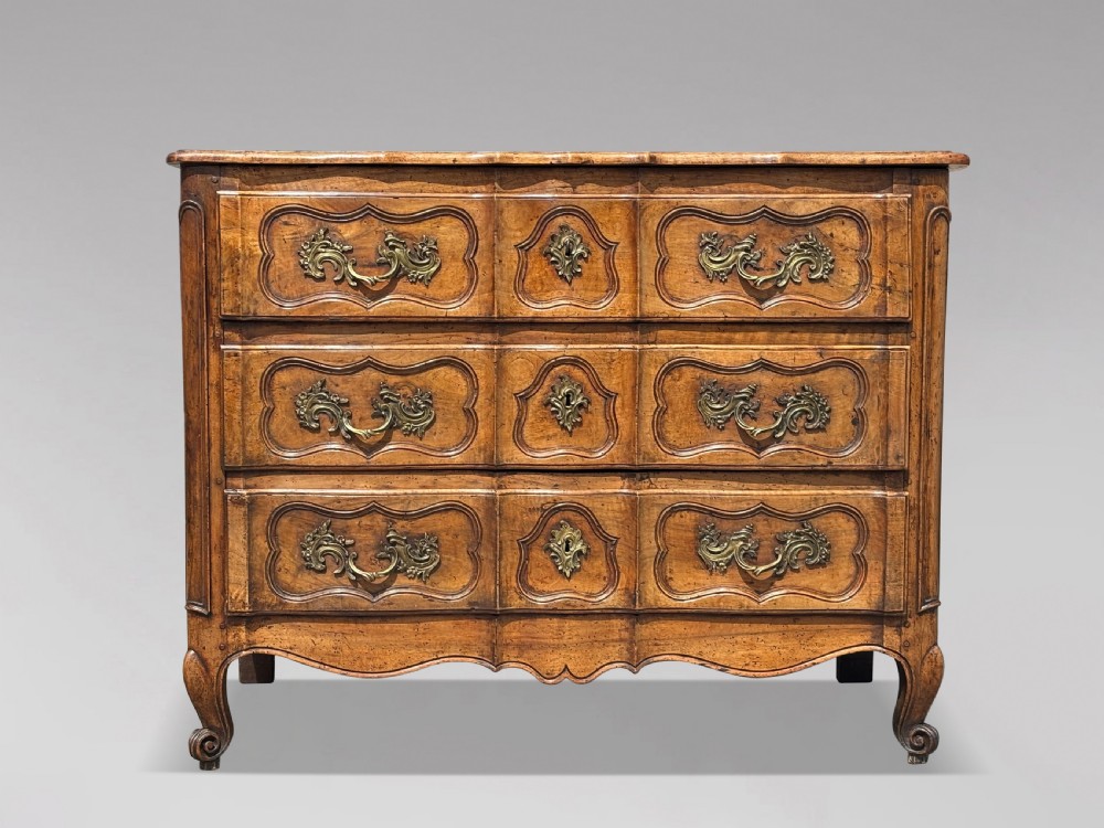 An eighteenth-century French Louis XV walnut commode featuring three carved drawers with rococo brass handles and cabriole legs.