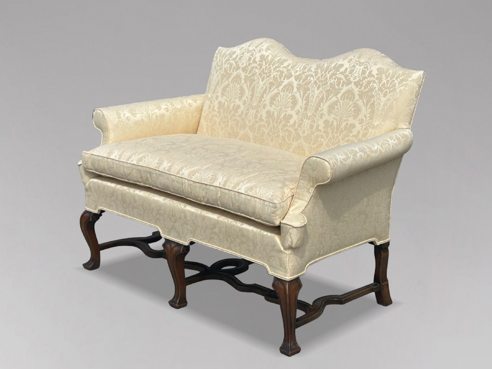 An Edwardian Queen Anne style settee upholstered in cream damask with carved walnut cabriole legs and a double-arched back. View II